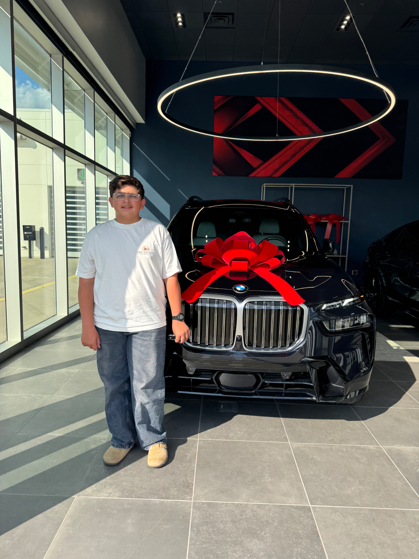 Liam, 13-year-old owner of Carolina Ride Care, standing next to a black BMW X7